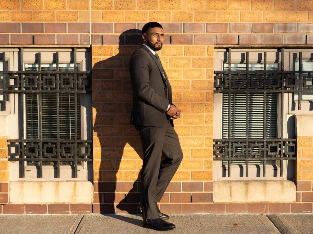 Kris Sidial, MCIT Online Student, wearing a suit, stands against building on a New York City sidewalk.